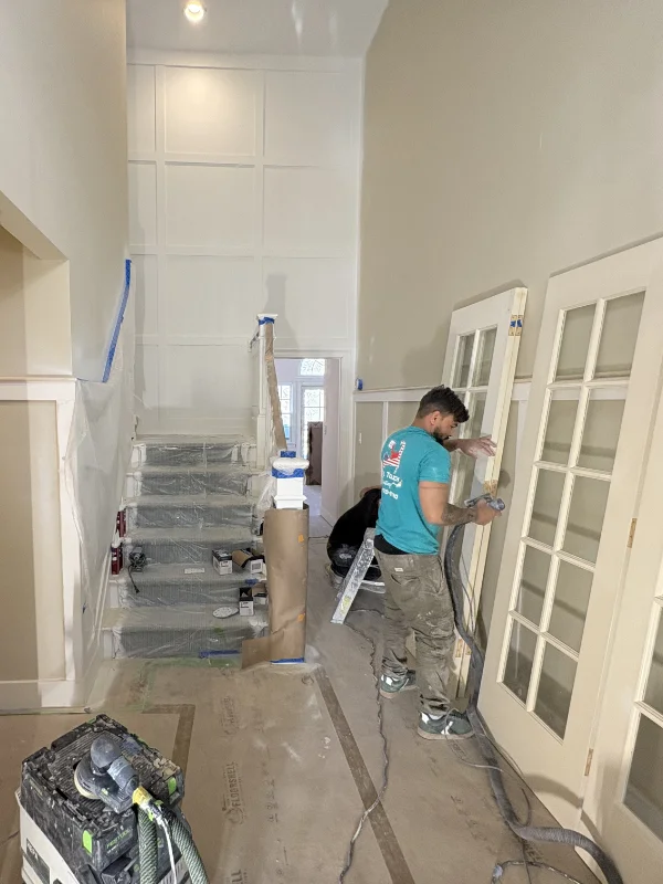 Professional exterior painter applying a protective white coating to Cape Cod shingle siding using a sprayer.