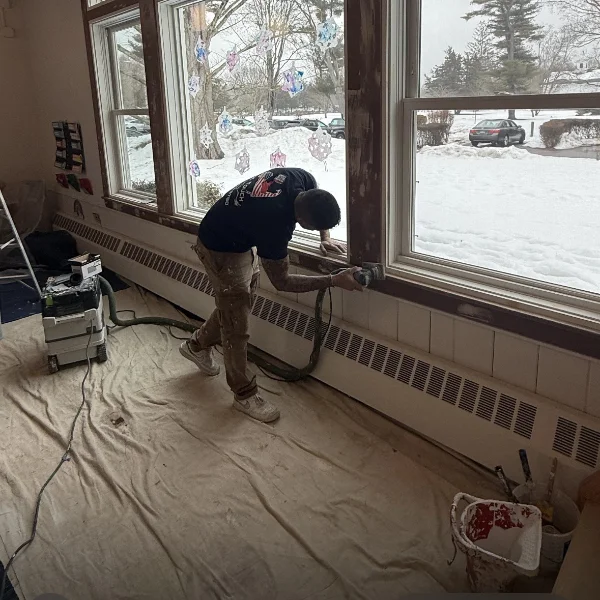 Close-up of a Final Touch master painter meticulously applying dark blue paint to interior wooden window trim.