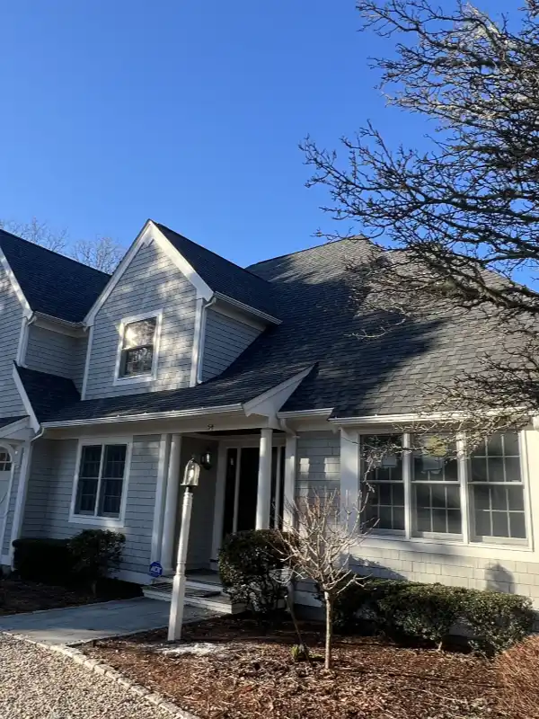 Coastal Cape Cod home featuring classic light gray siding and a newly installed dark gray roof