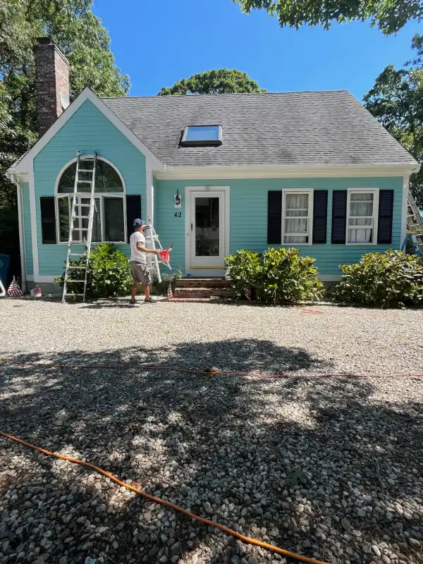 Professional painter carefully applying bright turquoise exterior paint on a residential home