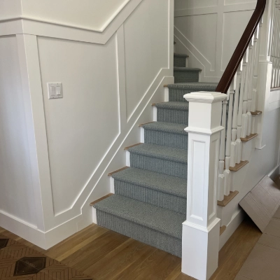 Staircase showcasing freshly painted white wainscoting and a patterned carpet runner