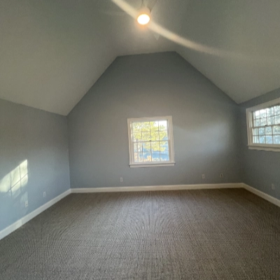 Spacious room with freshly painted light blue walls, a vaulted ceiling, and gray carpeting