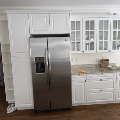 White refinished kitchen cabinets with glass doors surrounding a stainless steel refrigerator