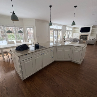 Large L-shaped kitchen island with white refinished cabinets and dark hardwood floors